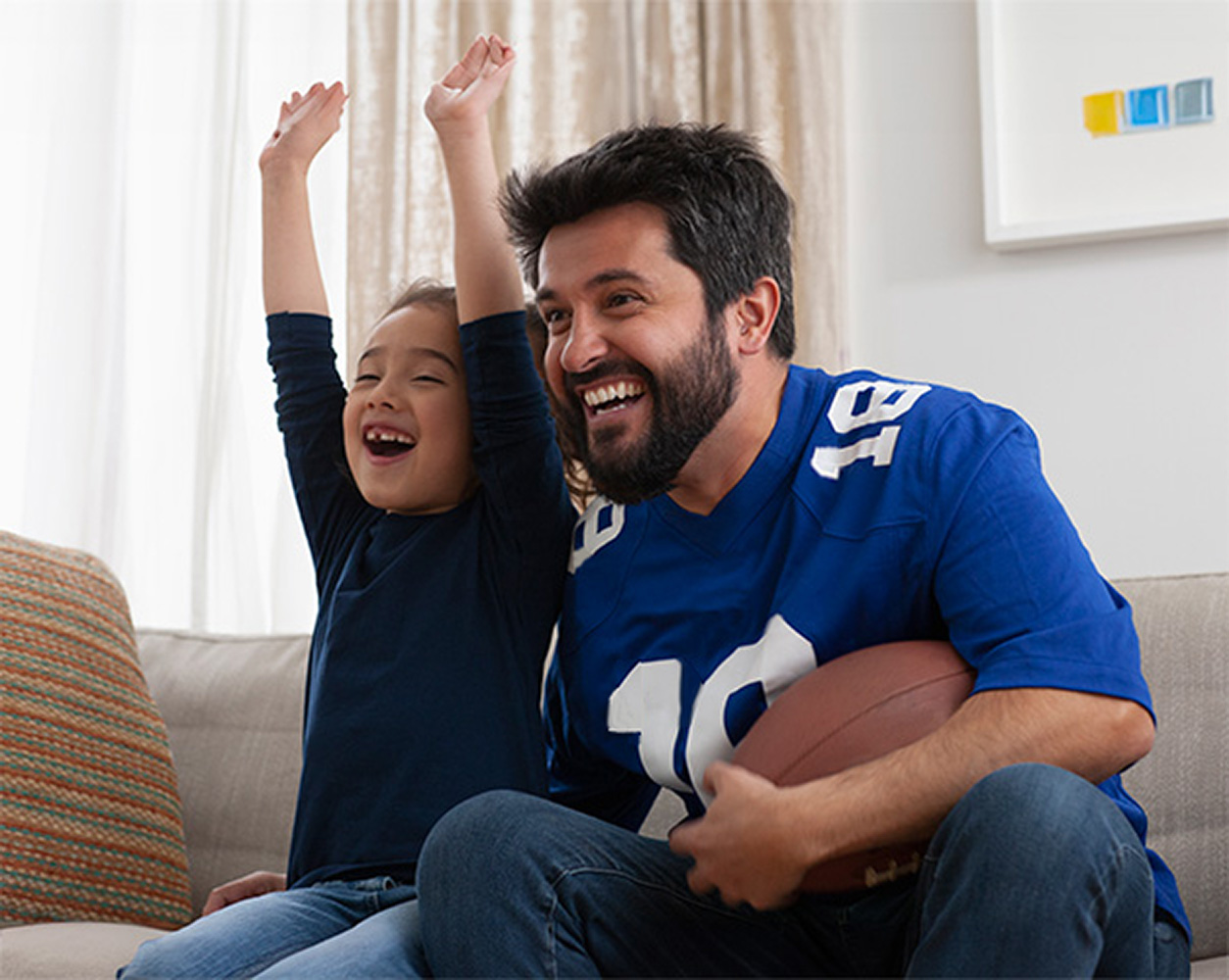 : A father and daughter watching football at home.