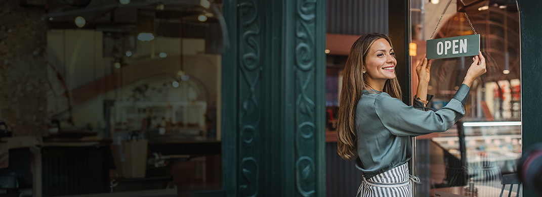 Woman hanging an open sign on the door of a business.