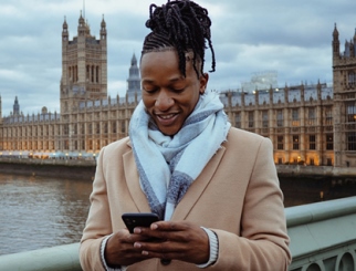 Una persona de pie frente al Palacio de Westminster de Inglaterra mientras consulta el teléfono.