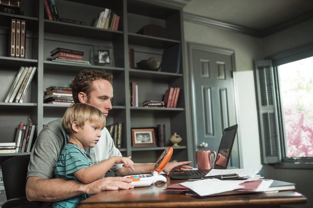 En la página 2024. Un padre y su hijo pequeño sentados en una oficina en casa miran sus computadoras.