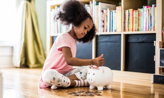 Little girl putting money in a piggy bank.