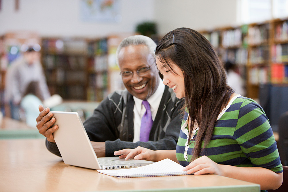 Older man and woman smiling at computer in a library