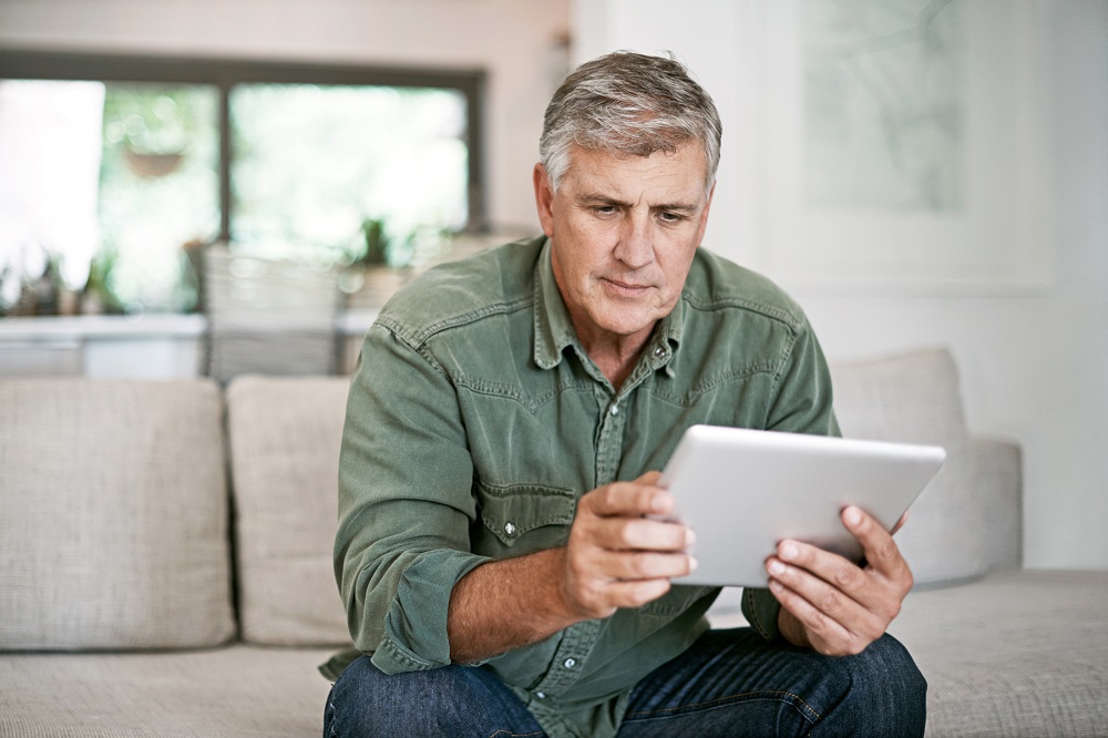 On-page, 2024. A middle-aged man looking seriously at a tablet in his hands while sitting on a couch.