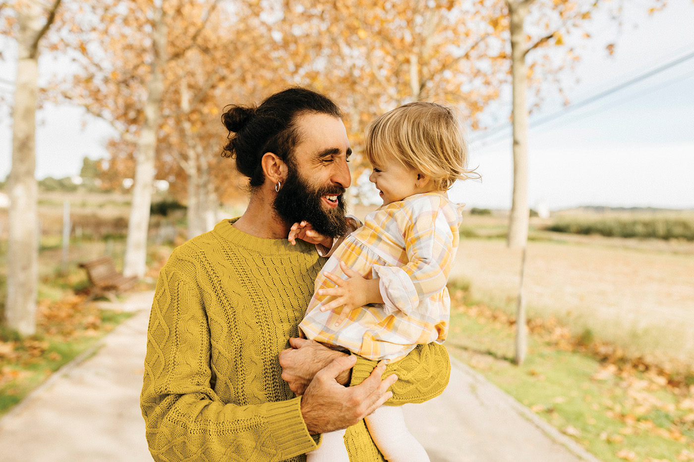 Un padre sonriente cargando a su hija en una mañana de otoño en el parque.