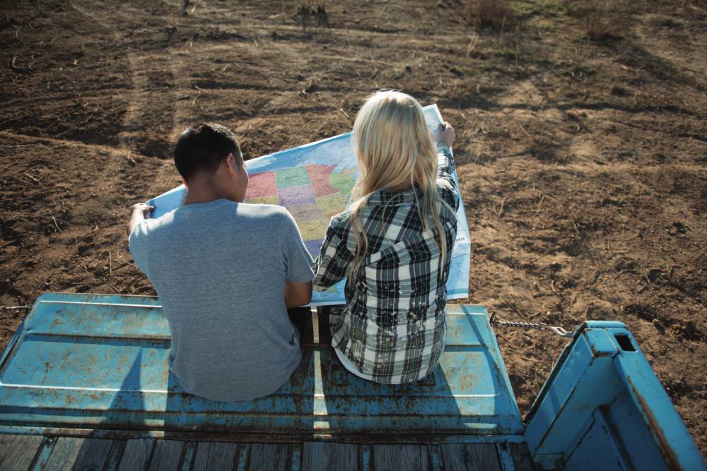 En la página 2024. Dos amigos sentados en la caja de un camión sostienen un mapa de los Estados Unidos.