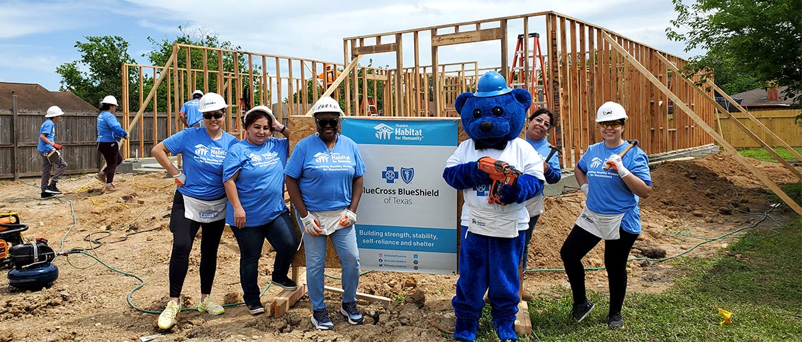 Employees of Blue Cross and Blue Shield of Texas stand in front of a Habitat for Humanity construction site