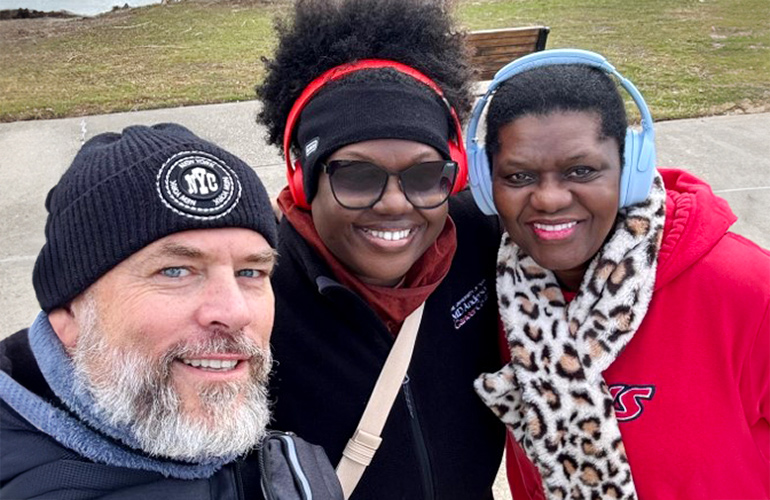 A bearded man with a ski cap and two women in ear muffs and scarves smile for a photo during a walk