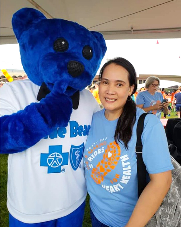 Woman poses with Blue Bear, the mascot for Blue Cross and Blue Shield of Texas, under a tent at an outdoor health event 