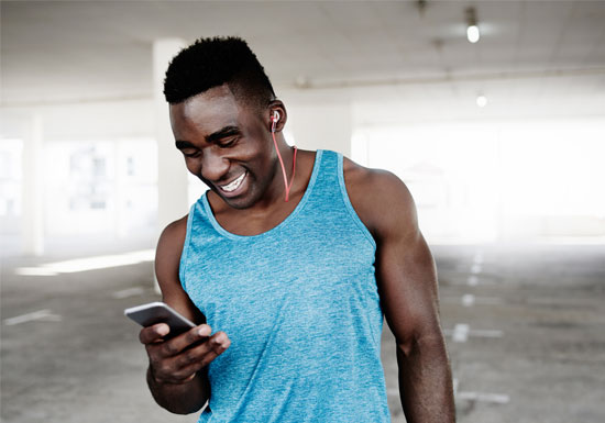 Athletic African American male using his mobile phone and wearing earbuds.