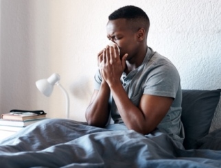 A young Man blowing his nose while sick in bed.